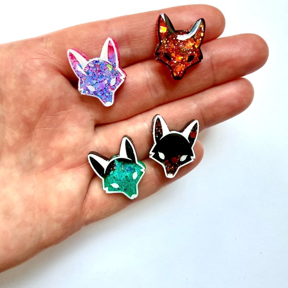Scale shot of handmade fox and wolf glitter resin pin badges held in hand by Copper Magpie Designs Liverpool UK