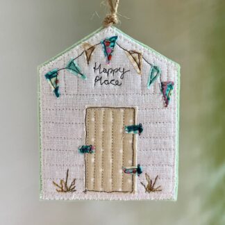 Hanging felt decoration of a beach hut with colourful bunting and a spotty door. The words happy place are stitched on the front