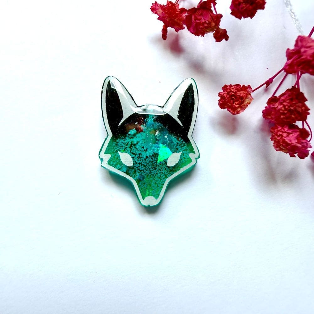 Teal galaxy glitter wolf resin pin badge handmade by Copper Magpie Designs Liverpool UK, displayed on a white background with pink flowers